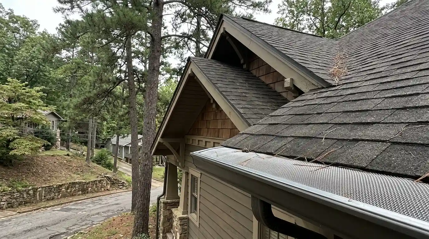 Micro-mesh gutter guards on a steep Craftsman home roof under tall pines on a hillside street in Hot Springs Arkansas